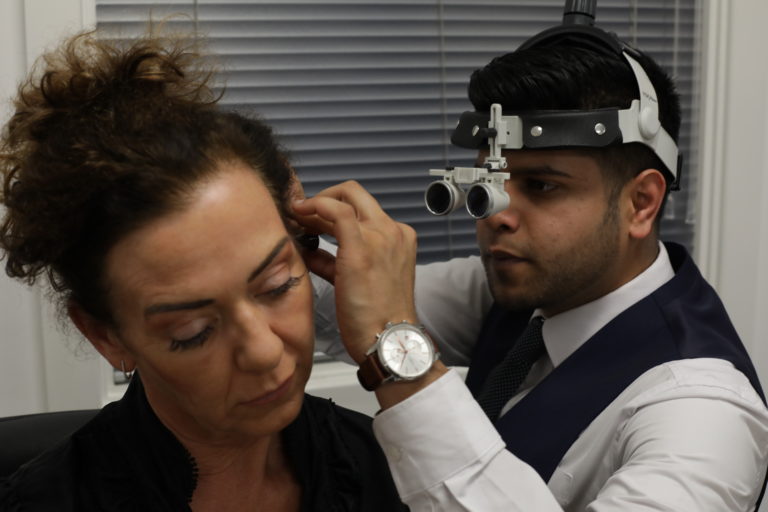 A professional audiologist using magnifying loupes to perform a precise microsuction ear wax removal procedure on a patient.