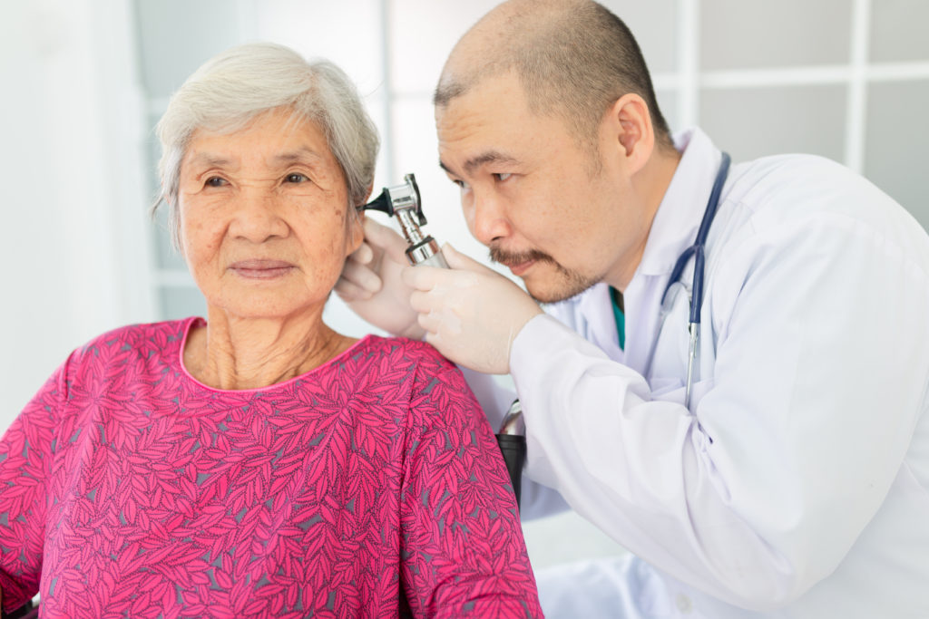 Audiologist inspecting elderly woman ear canal