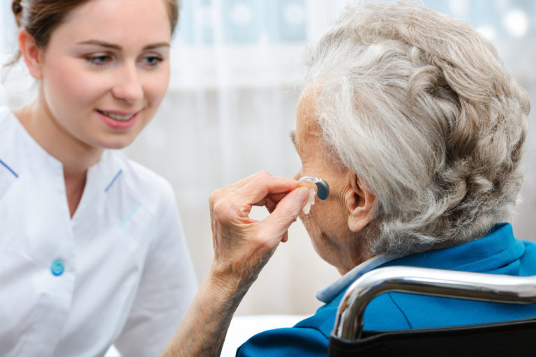 A clinician in a white coat performing an otoscopy exam on a patient's ear using a handheld otoscope to check for ear health and hearing loss.