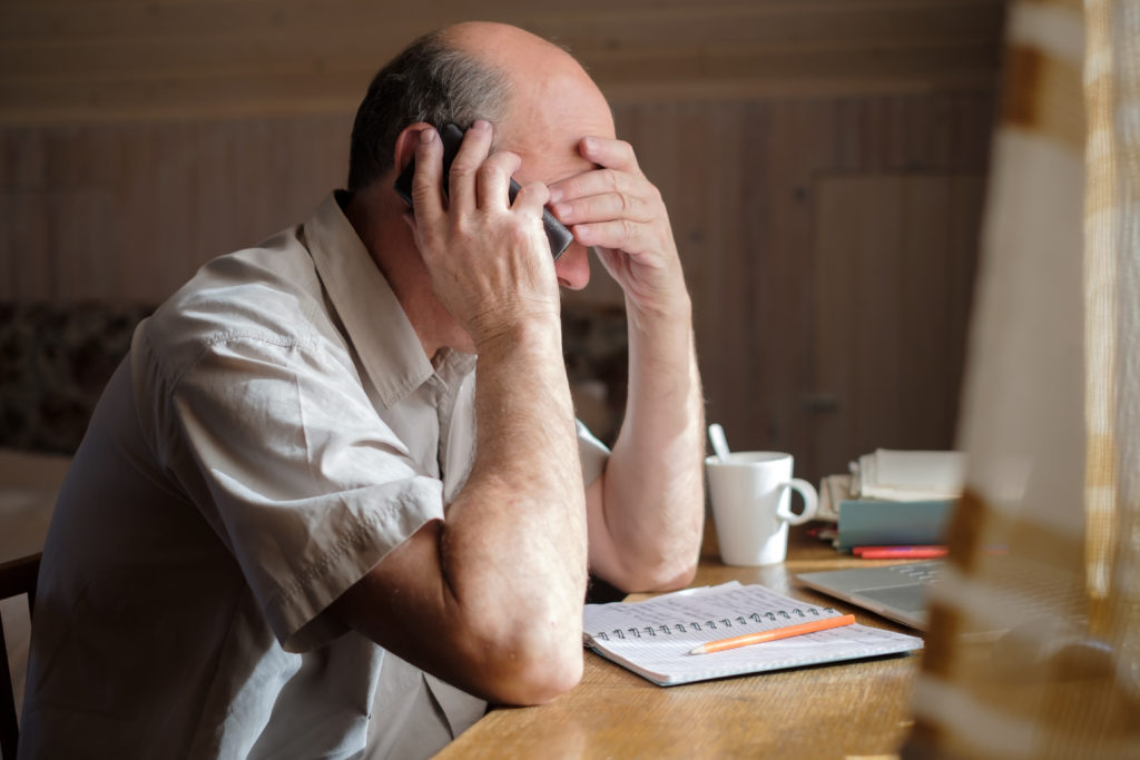 Elderly man sat on the phone with his head in his hands