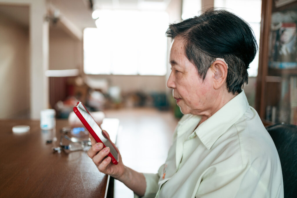 Elderly woman with hearing aid using a smartphone for video call at home.